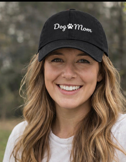 Woman smiling wearing a black denim hat  that says dog mom with a paw print in-between the dog and mom  