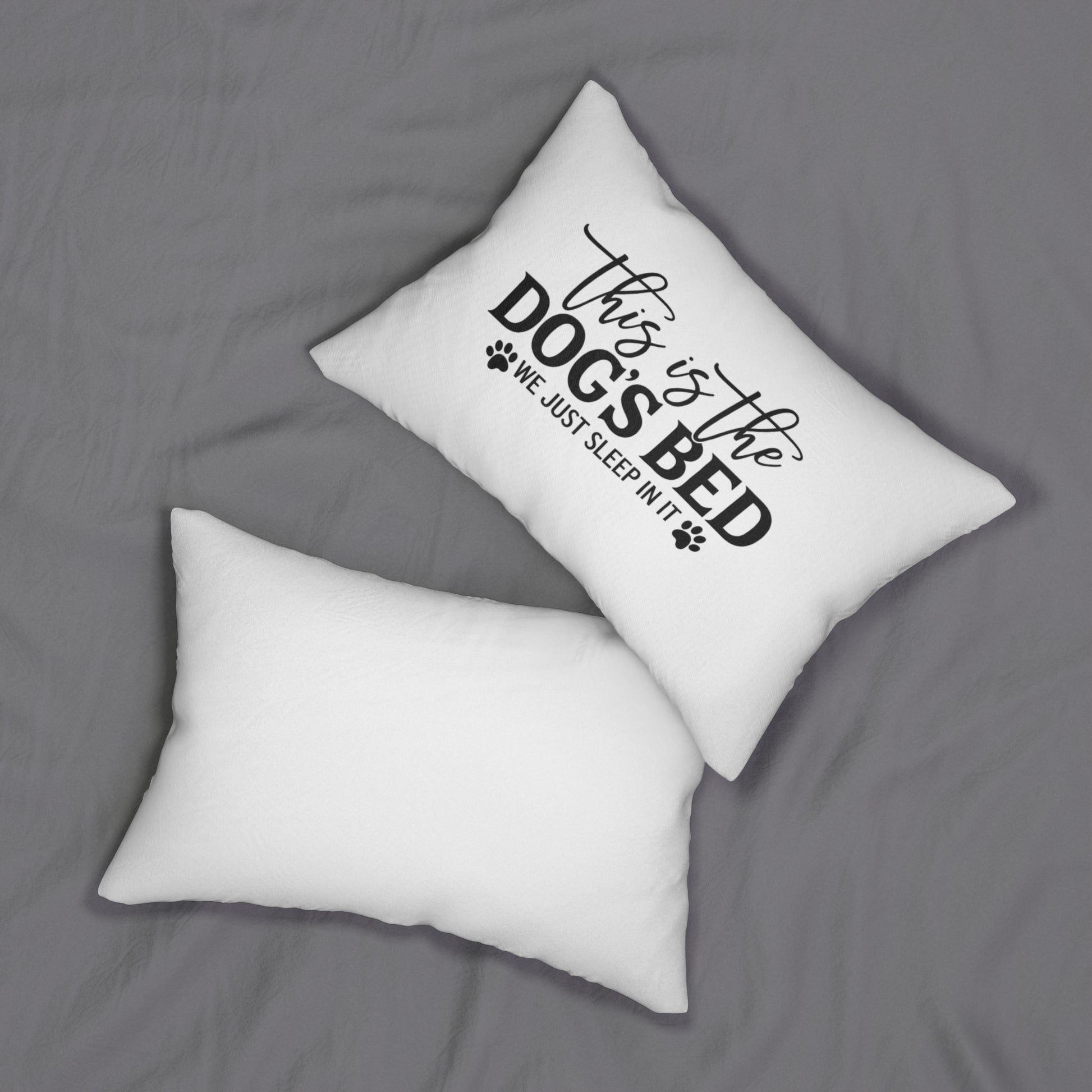 Two white pillows on a gray surface with one pillow featuring black text saying this is the dogs bed we just sleep in it 