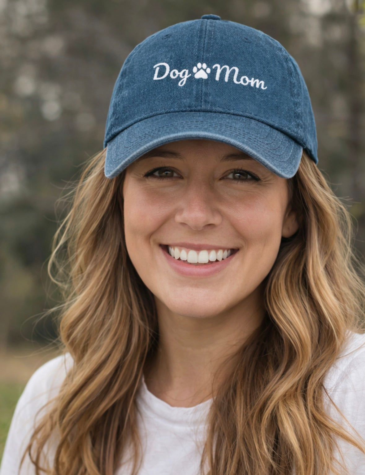 Woman smilig outside while  wearing a blue denim hat with embroidered  'Dog Mom' text on the front of the hat.